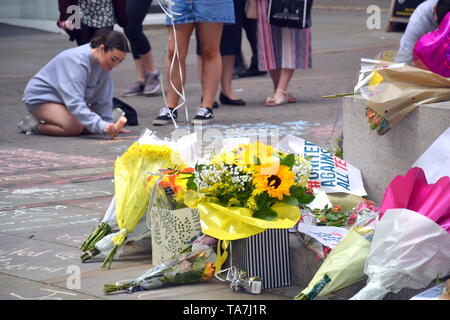 22nd mai 2019. Commémoration du deuxième anniversaire de l'attentat terroriste à la bombe de Manchester Arena qui a fait 22 morts : une jeune femme craie un message sur le monument commémoratif de la rue à la place St Ann, Manchester, Royaume-Uni. Banque D'Images