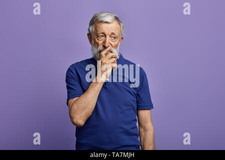 Vieux homme attentionné avec une main sur sa bouche à côté. la photo en gros. isolé sur fond bleu.idée, plan, mature man résoudre un problème , isoler Banque D'Images