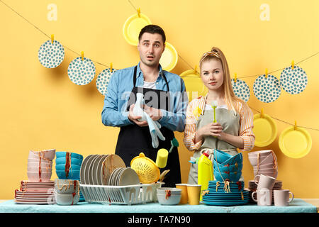 Serious attractive blonde femme avec brosse et surpris homme tenant une serviette et la plaque derrière la table et regardant la caméra. natures mortes Banque D'Images