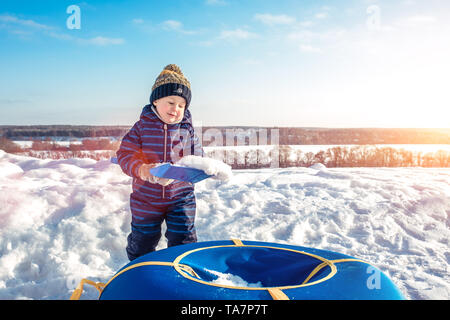Un petit garçon joue dans l'hiver à l'extérieur avec de la neige, d'une pagaie de tubes gonflables pour le ski. Vêtements chauds pour l'hiver et un chapeau. Espace libre pour le texte. Banque D'Images