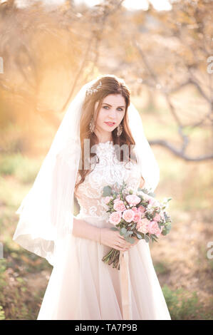 Belle bride holding bouquet standing outdoors. En regardant la caméra. Jour de mariage. La célébration. 20s. Banque D'Images