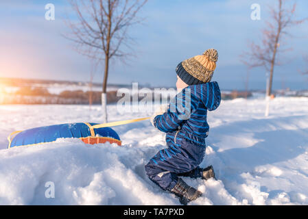 Un petit garçon de 3 ans, en hiver sur la rue tire un tube, pour le ski d'une colline, s'amusant à jouer le week-end de détente, la neige fond Banque D'Images