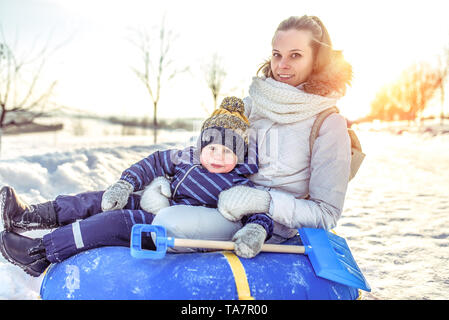 Belle mère femme avec bébé garçon 3 ans, assis tubes gonflables, roulant vers le bas de la colline, après avoir reste, l'hiver sur un week-end en plein air Banque D'Images