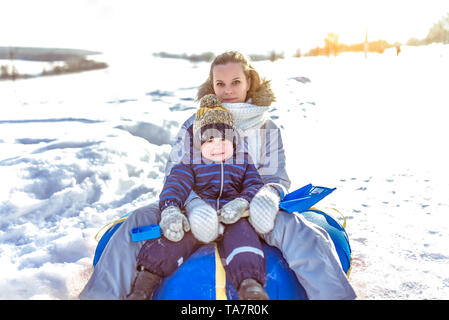 Maman femme avec enfant garçon 3 ans, assis sur un tube gonflable, rouler glisser dans l'air frais d'hiver repos vacances week-end resort, l'arrière-plan Banque D'Images