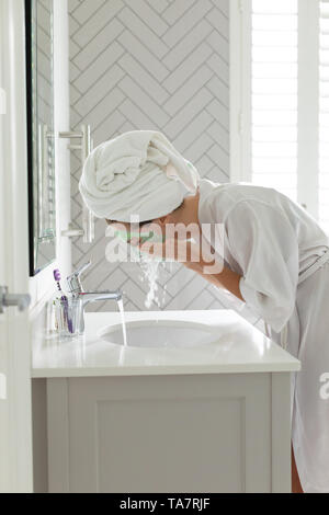 Laver sa femme masque de visage à l'évier de salle de bains à la maison Banque D'Images