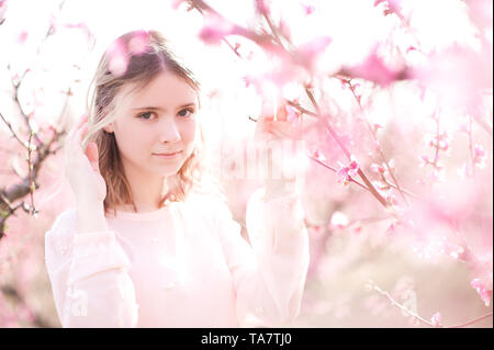 Smiling blonde Fille 16-17 ans posant en gros plan fleurs rose pêche à l'extérieur. En regardant la caméra. La saison du printemps. Banque D'Images