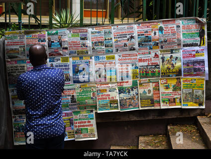 Homme africain lire les journaux affichés sur un étal de marché, Région des lagunes, Abidjan, Côte d'Ivoire Banque D'Images