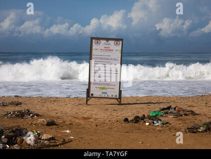 Des ordures sur la plage en face d'un billboard pour lutter contre la pollution, Sud-Comoé, Grand-Bassam, Côte d'Ivoire Banque D'Images