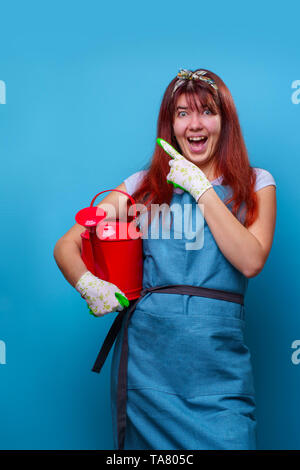 Image of female florist avec arrosoir en mains de doigt à l'autre sur fond bleu vide. Banque D'Images