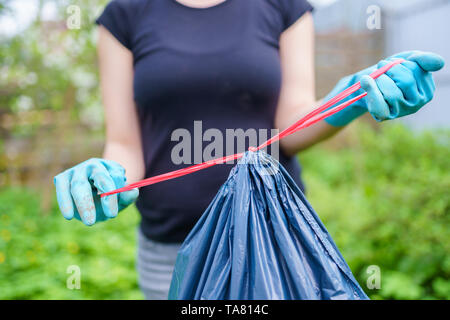 Photo de femme dans les gants en caoutchouc avec un sac poubelle sur le jardin en été Banque D'Images