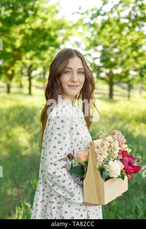 La moitié d'un portrait positif de charme femme vêtue de longues robes blanches avec un sourire heureux sur le fond d'un pré vert dans les mains de Banque D'Images