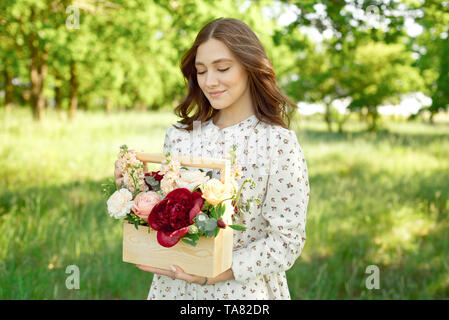 La moitié d'un portrait positif de charme femme vêtue de longues robes blanches avec un sourire heureux sur le fond d'un pré vert dans les mains de Banque D'Images