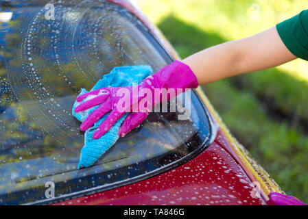 Femme dans les gants en caoutchouc se lave une voiture rouge. Détergent de nettoyage Banque D'Images