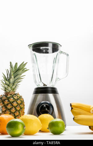 Low angle view of blender près de bananes jaunes mûres, ananas, citron, orange et citron vert sur blanc Banque D'Images