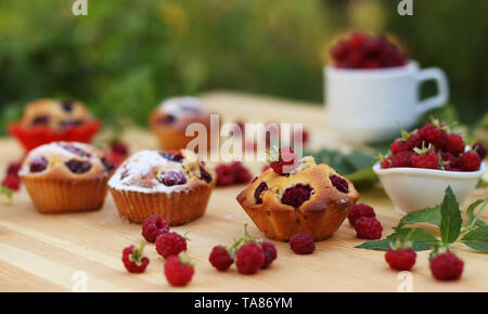 Muffins aux framboises sont situés sur une table en bois sur l'arrière-plan de buissons verts, autour de beaucoup de framboises fraîches Banque D'Images