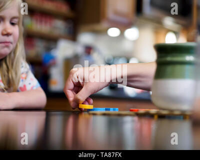Les mères d'une part prend les lettres en plastique en mots sur une table de cuisine tandis que les jeunes fille ressemble à du bord du cadre. Shallow DOF. Banque D'Images