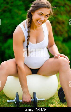 Smiling pregnant woman Lifting Dumbbells tout en restant assis sur le Yoga Ball Banque D'Images