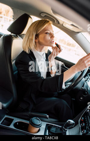 Belle blonde young woman applying lipstick while sitting in car Banque D'Images