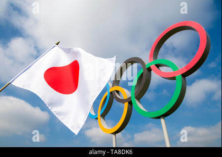 Londres - Avril 2019 : Un drapeau japonais qui oscille au vent en face d'anneaux olympiques sous ciel bleu. Banque D'Images