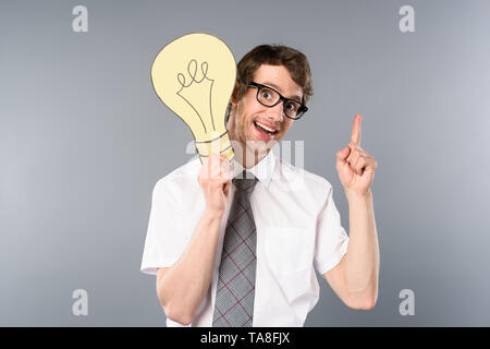 Smiling businessman in glasses holding coupe papier jaune ampoule et montrant idée geste sur fond gris Banque D'Images