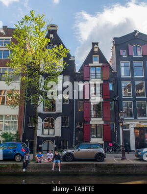 Les touristes s'asseoir le long d'un canal à Amsterdam Pays-Bas avec canal étroit maisons derrière eux Banque D'Images