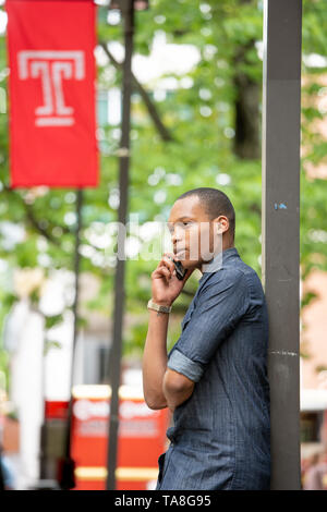 Young African American man in Philadelphia, marche sur le campus de l'Université Temple sur son téléphone Banque D'Images