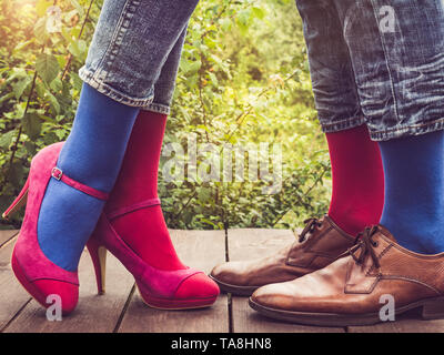 Les hommes et les femmes chaussures à la mode dans les jambes, lumineux, chaussettes multicolores sur une terrasse en bois sur l'arrière-plan de vert des arbres et de la lumière du soleil. Close-up. Banque D'Images