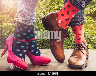 Les hommes et les femmes chaussures à la mode dans les jambes, lumineux, chaussettes multicolores sur une terrasse en bois sur l'arrière-plan d'arbres verts et des rayons de soleil. Close-up Banque D'Images