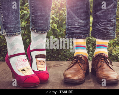 Les hommes et les femmes chaussures à la mode dans les jambes, lumineux, chaussettes multicolores sur une terrasse en bois sur l'arrière-plan de vert des arbres et de la lumière du soleil. Close-up. Banque D'Images