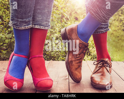 Les hommes et les femmes chaussures à la mode dans les jambes, lumineux, chaussettes multicolores sur une terrasse en bois sur l'arrière-plan de vert des arbres et de la lumière du soleil. Close-up. Banque D'Images