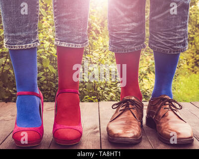 Les hommes et les femmes chaussures à la mode dans les jambes, lumineux, chaussettes multicolores sur une terrasse en bois sur l'arrière-plan de vert des arbres et de la lumière du soleil. Close-up. Banque D'Images