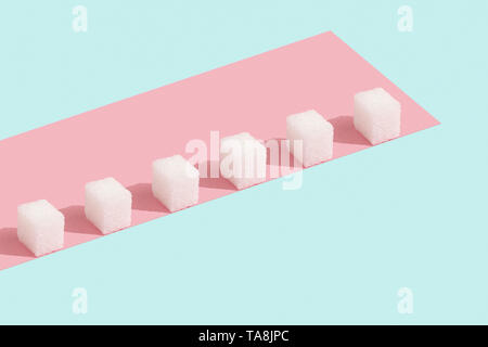 Morceaux de sucre dans une rangée sur fond rose et bleu. Couleurs tendance pastel. Un style minimaliste. Banque D'Images