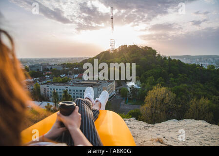 Femme regardant le coucher du soleil sur la ville. boire du café. assis sur le pic Banque D'Images