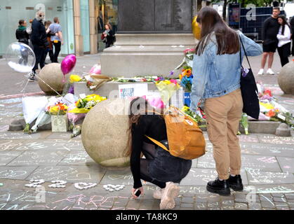 22nd mai 2019. Commémoration du deuxième anniversaire de l'attentat terroriste à la bombe de Manchester Arena qui a fait 22 morts : une jeune femme craie un message sur le monument commémoratif de la rue à la place St Ann, Manchester, Royaume-Uni. Banque D'Images