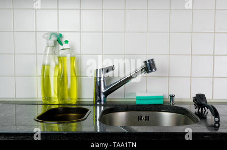 Et le robinet d'évier de cuisine avec une éponge et un pinceau sur un dessus de table en granit noir et jaune liquide vaisselle nettoyant cuisine et derrière Banque D'Images