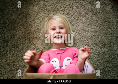 Un peu heureux 3 ans enfant dans son pyjama, rit alors qu'elle joue dans une boîte carton, à son domicile. Banque D'Images