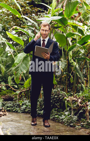 Happy businessman en costume et lunettes en conversation sur smartphone et du dossier en vous promenant dans les émissions de Banque D'Images