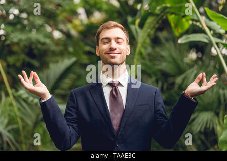 Handsome smiling businessman en costume et cravate aux yeux clos méditant dans orangerie Banque D'Images