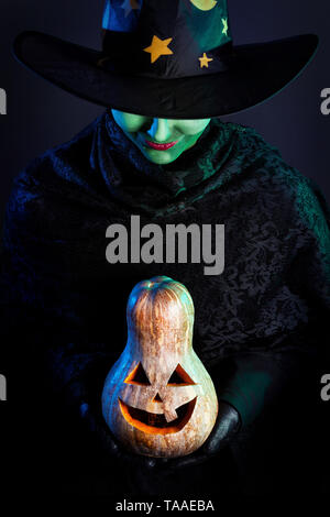 Sorcière avec peau verte holding carved Halloween Pumpkin lantern fond sombre Banque D'Images