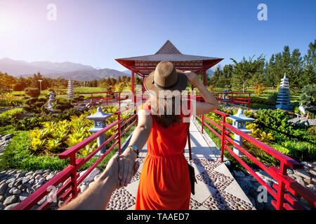 Femme en robe orange et hat holding man à la main aller à la pagode avec jardin japonais Banque D'Images