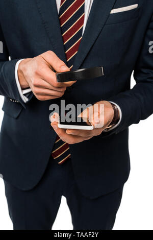 Portrait of businessman in suit holding smartphone près de loupe isolated on white Banque D'Images