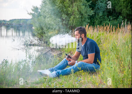 Confiant fumeur reposant sur la nature et le tabagisme La fumée électronique périphérique. Vaping concept. Banque D'Images