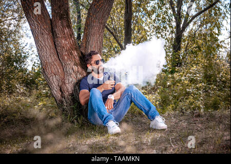 Confiant vaper explose un couple un vape sur le sol forestier. Cigarette électronique concept. Banque D'Images