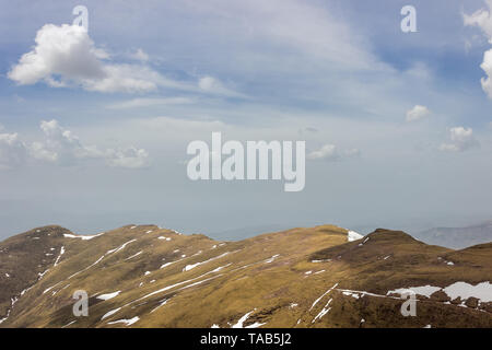 Ciel bleu avec des nuages blancs sur les hautes terres et les prairies ensoleillées de vieille montagne avec des pics pointus et de neige qui reste au début du printemps Banque D'Images