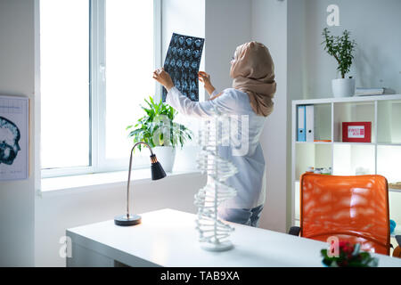 Près de la table de travail. Femme scientifique médicale portant foulard, debout près de la table de travail et à la recherche à x-ray Banque D'Images