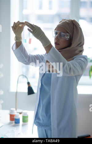 L'étude des liquides chimiques. Jeune femme portant des lunettes et des gants de chimiste de l'étude des liquides chimiques Banque D'Images