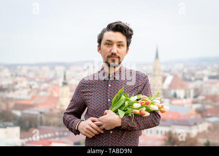 Portrait d'un beau jeune homme avec des fleurs de tulipe. Concept d'un homme tenant des fleurs tulipes comme cadeau pour une occasion spéciale . Banque D'Images