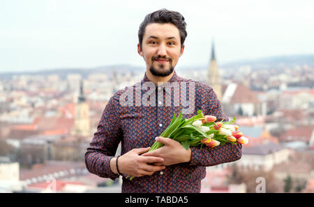 Portrait d'un beau jeune homme avec des fleurs de tulipe. Concept d'un homme tenant des fleurs tulipes comme cadeau pour une occasion spéciale . Banque D'Images