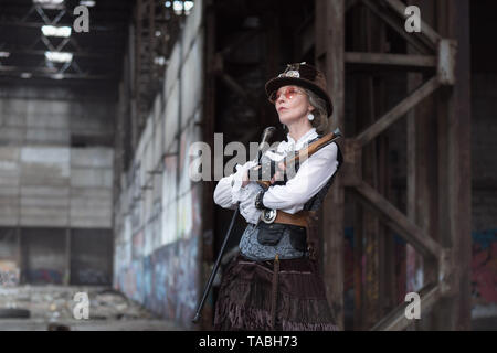 Dame âgée dans un costume steampunk dans une usine abandonnée les armes à la main. Banque D'Images