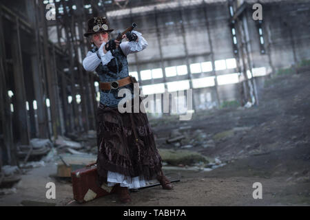 Dame âgée dans un costume steampunk dans une usine abandonnée les armes à la main. Banque D'Images